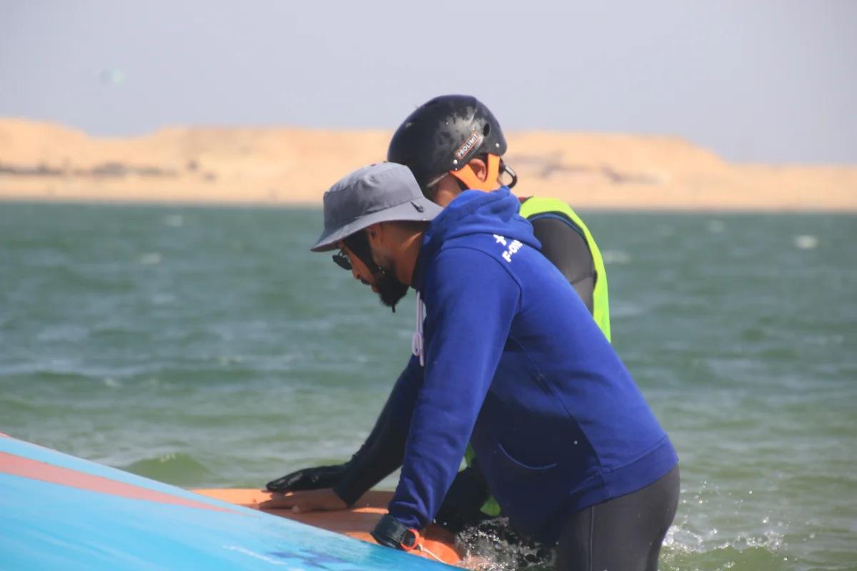 Instructeur wingfoil Bluboarding expliquant à un élève où se positionner sur une planche à foil avant d'aller dans l'eau