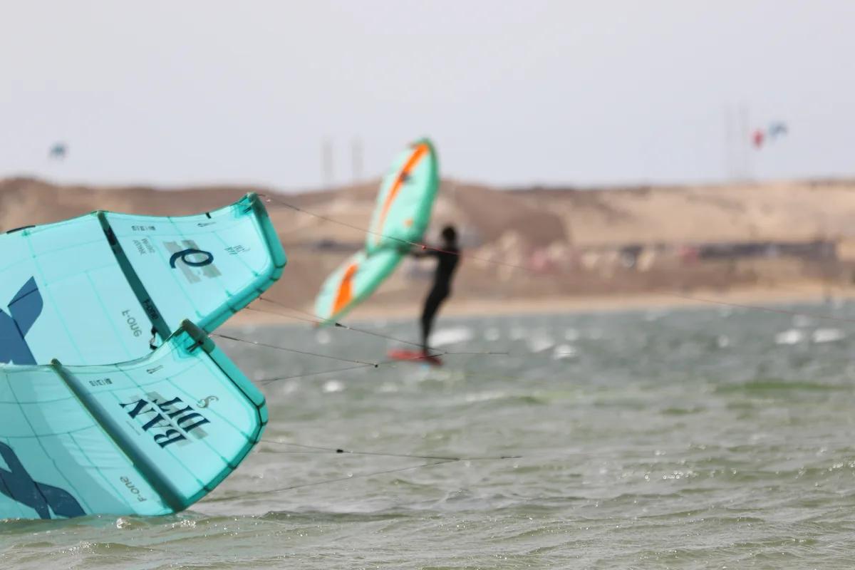 Client wingfoil Bluboarding en location passant devant un kitesurfeur utilisant du matériel de location sur le lagon de Dakhla, illustrant l'option location combo.