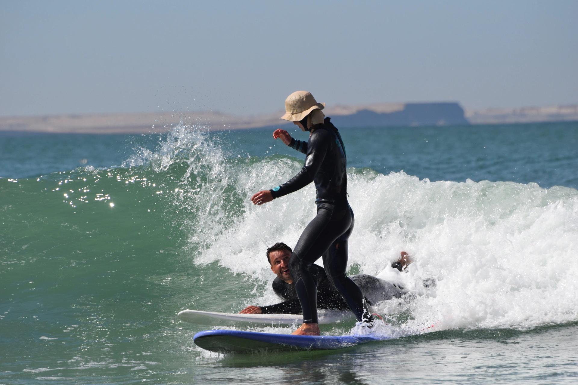Un couple souriant attrapant une vague ensemble lors d'un cours de surf Bluboarding sur les breaks océaniques près de Dakhla.