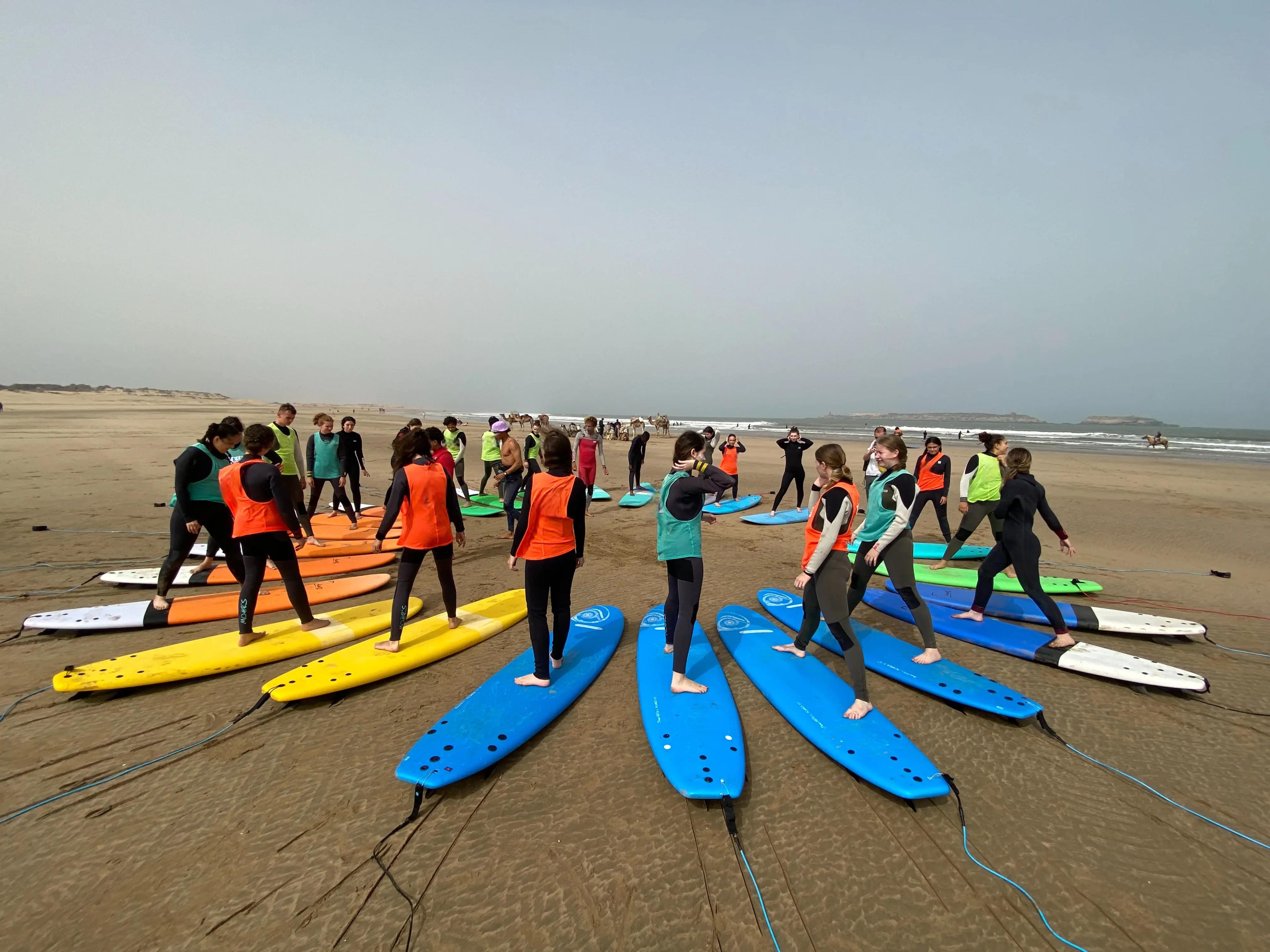 Groupe d'élèves surf Bluboarding s'entraînant à la posture sur la plage de sable d'Essaouira lors d'un cours de surf collectif au Maroc.