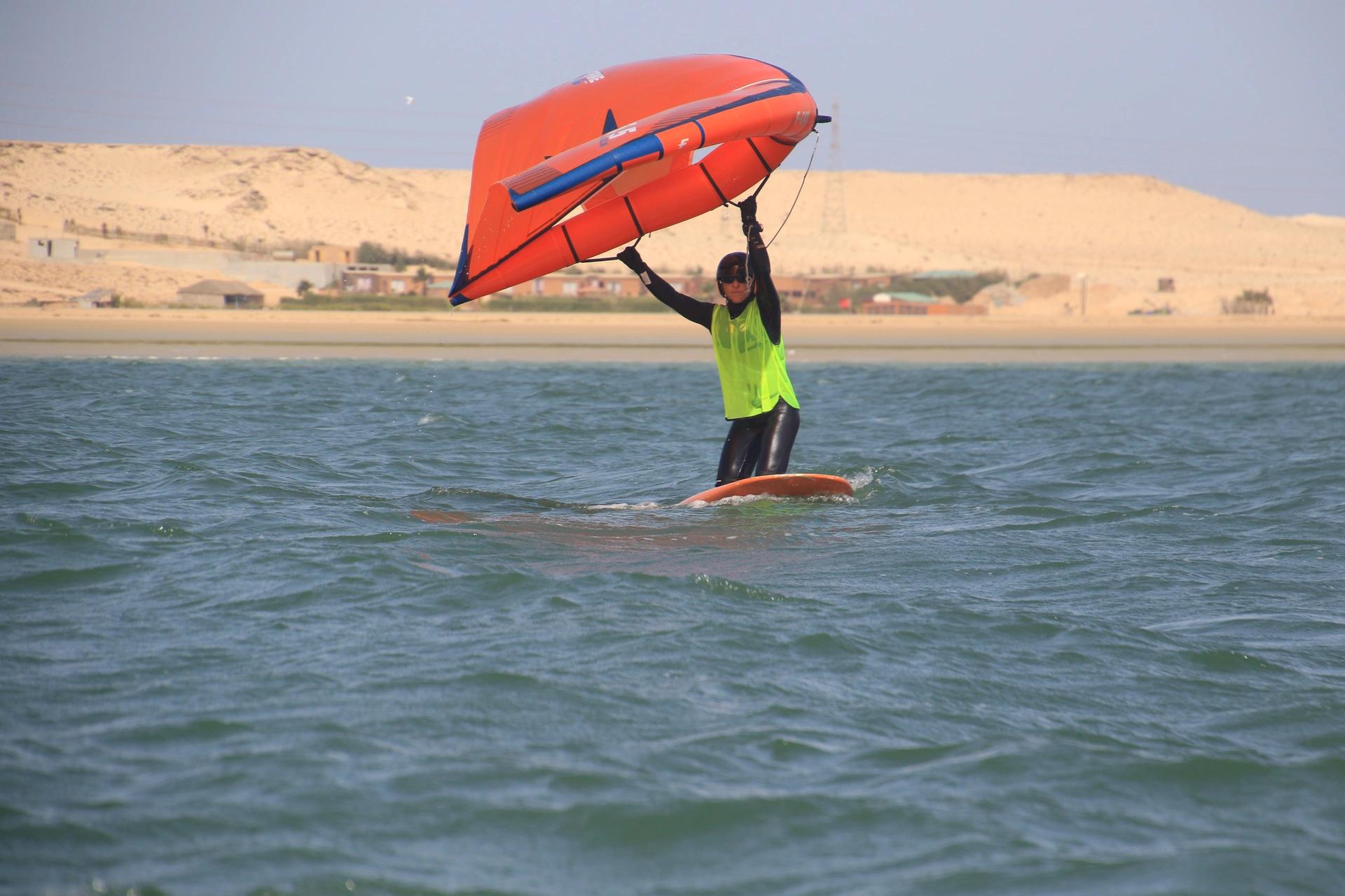 Bluboarding wingfoil student kneeling on the board and practising wing control in the flat water of the Dakhla lagoon during a wingfoil lesson in Morocco.