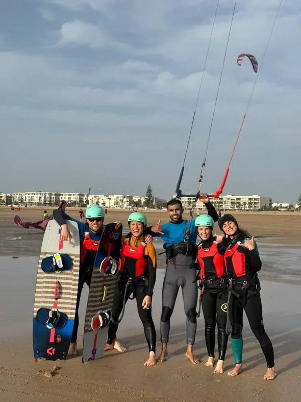 Groupe joyeux de clients kitesurf Bluboarding posant avec leur moniteur sur la plage d'Essaouira pour une photo souvenir après un cours collectif.