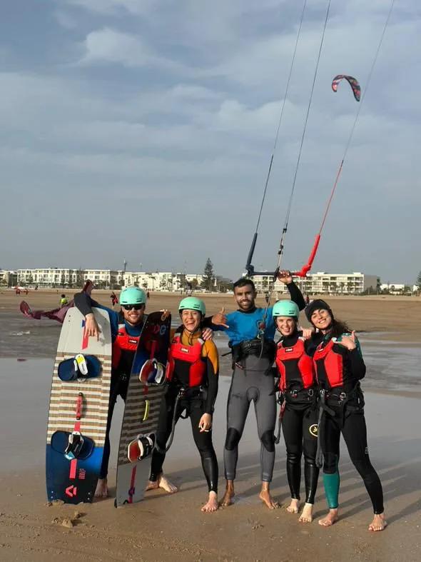 Bluboarding instructor posing with four happy kitesurf students on the beach of Essaouira after a group kitesurf lesson in Morocco.