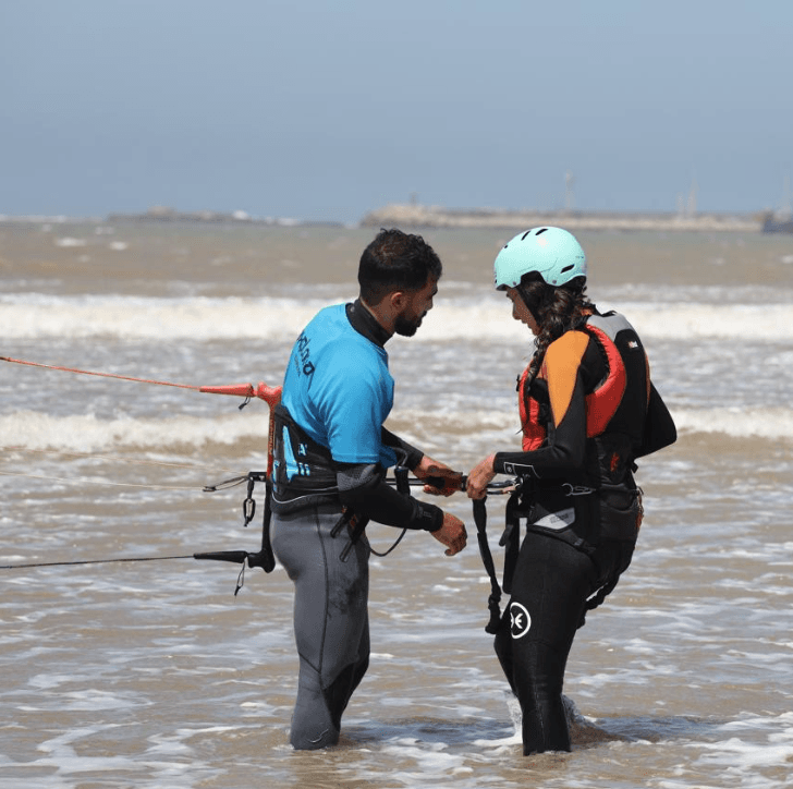 Moniteur kitesurf Bluboarding aidant une cliente à accrocher le kite avant son waterstart sur la plage principale d’Essaouira.
