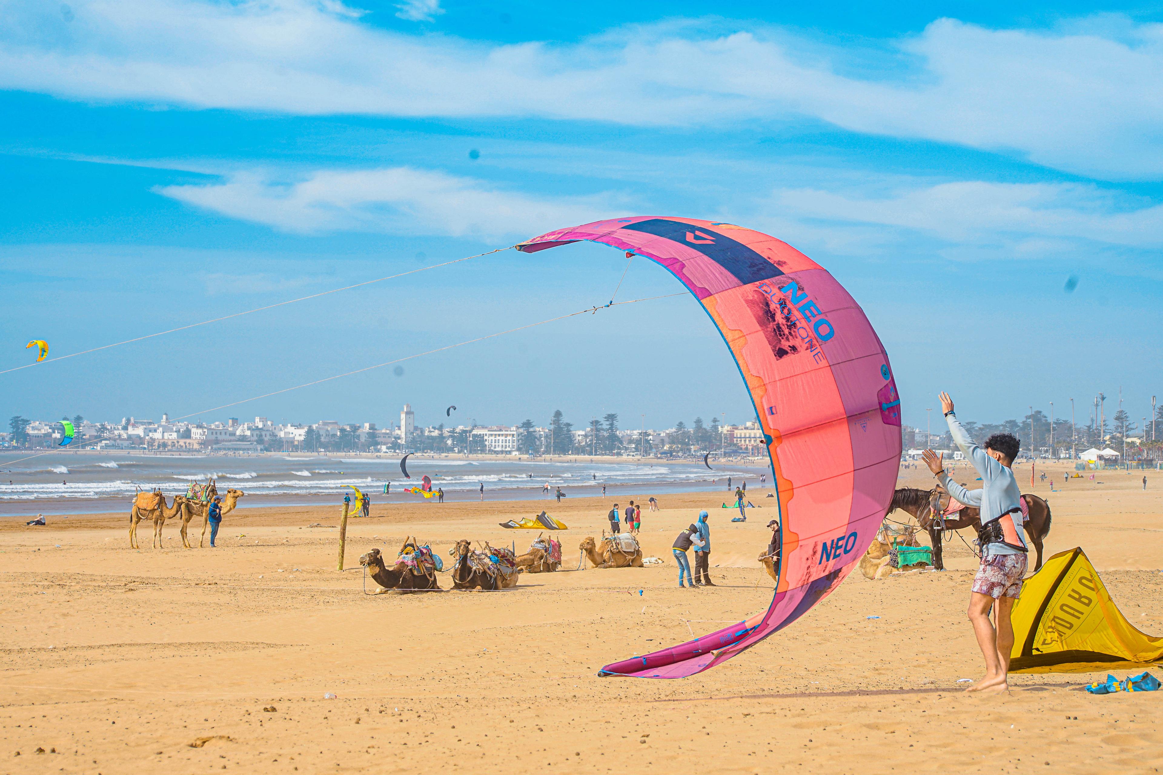 Membre de l'équipe Bluboarding aidant un client à lancer le kite sur la large plage de sable d'Essaouira avant un cours de kitesurf.