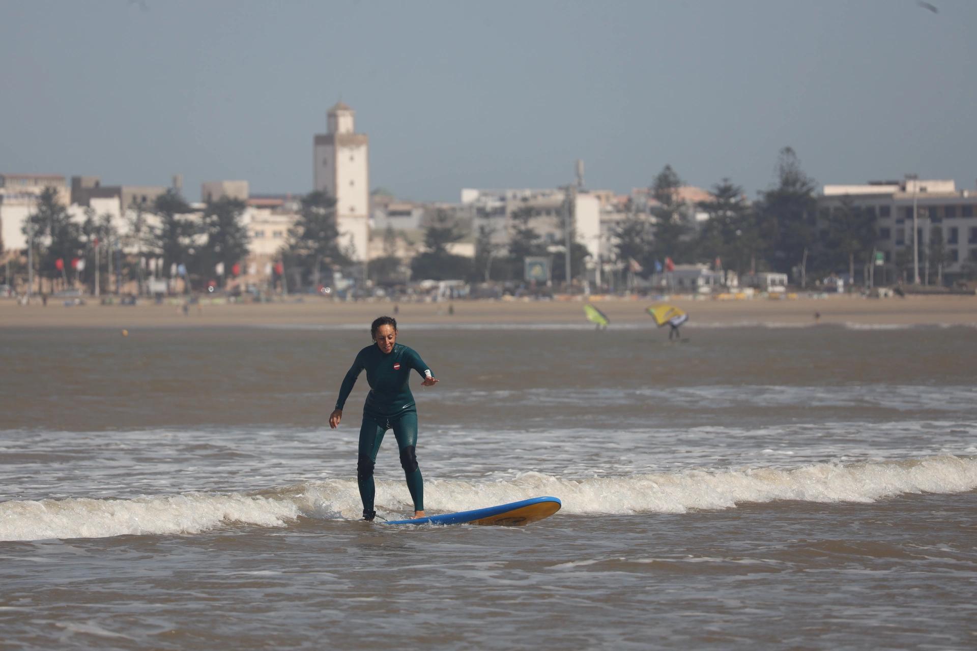 Cliente Bluboarding attrapant une petite vague avec le sourire lors d’un cours de surf sur la plage principale d’Essaouira.