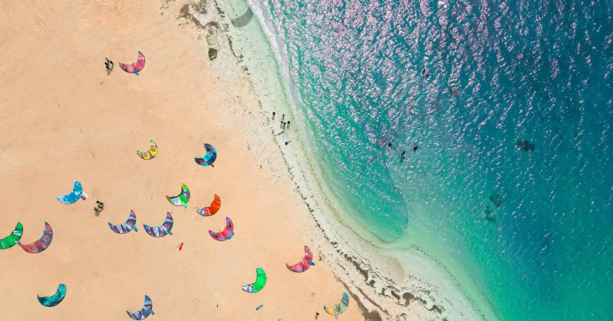 Aerial view of the Dakhla lagoon in Morocco showing turquoise flat water and colorful kites resting on the golden sandy beach, a world-class kitesurfing and wingfoil destination.